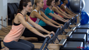 Women participating in a Pilates class using reformer machines, lined up in a studio.